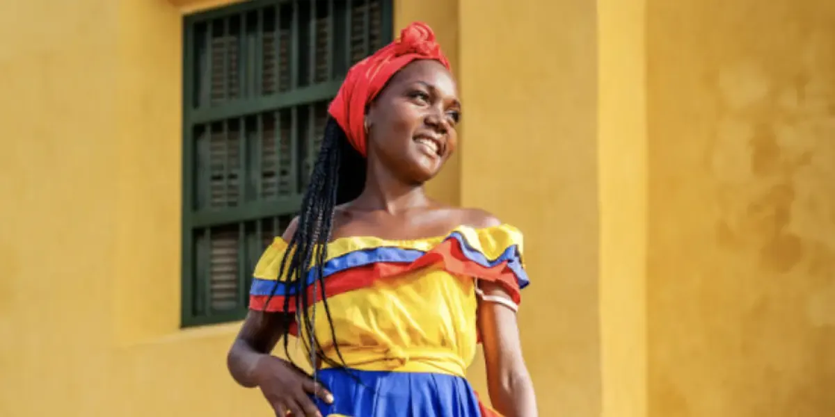 Mujer afro sonriente con una pañoleta roja sobre su cabeza y con un vestido con los colores de Colombia